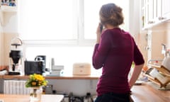 A young woman at home in the kitchen is using a telephone