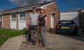 Graham and Lisa stand with their arms round each other with their dog on the driveway of. a brick bungalow