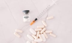 A glass vial with a white label saying "fentanyl" alongside a syringe with an orange tip and many white pills, on a white marble counter.