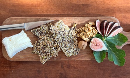 A wedge of soft cheese, crispbread, fresh figs and walnuts on a wooden board.