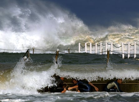 Young boys crouch behind an ocean pool wall as they play in the massive surf at Sydney’s Narrabeen beach.