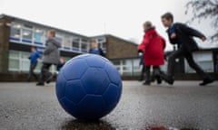 A football lying on the ground in a playground, with children playing in the background, out of focus