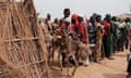 Two children suffering from malnutrition sit on an emaciated donkey next to a line of people