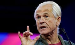 Older white man with longish white hair wearing an olive cardigan gestures as he speaks on a stage.