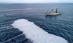 A ship and a small dinghy next to a white mass on the sea  perhaps 100 metres long of dead fish