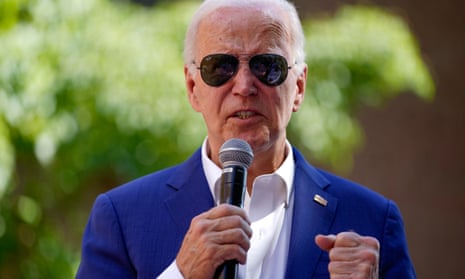 white man wearing sunglasses and blue suit holds microphone