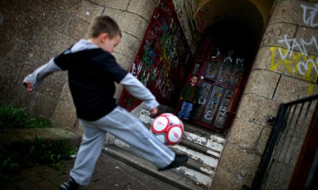 Boys play football in a run-down street with boarded up houses in the Govan area of Glasgow