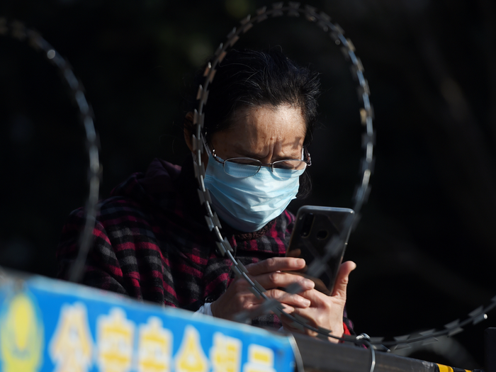 FILE PHOTO: A woman uses her mobile phone behind barbed wire at an entrance of a residential compound in Wuhan, the epicentre of the novel coronavirus outbreak, Hubei province, China February 22, 2020. REUTERS/Stringer/File Photo