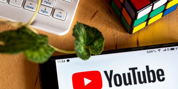 A YouTube photo illustration with the site's logo visible on a phone screen next to a Rubik's cube and computer keyboard on a desk