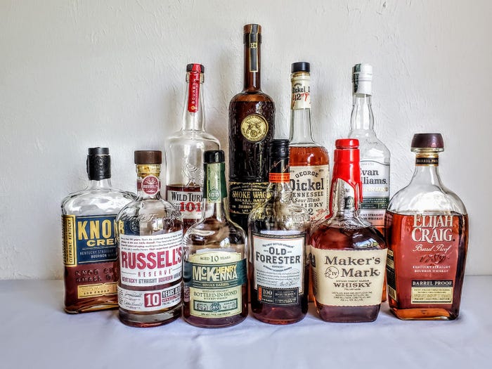 A cluster of ten bourbon bottles from an assortment of brands sits on a table.