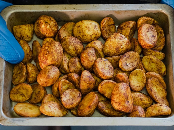 Woman in apron holding platter of roasted potatoes.