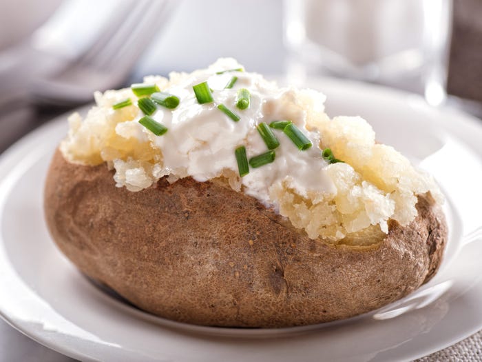 A baked potato cut open and topped with sour cream and chives