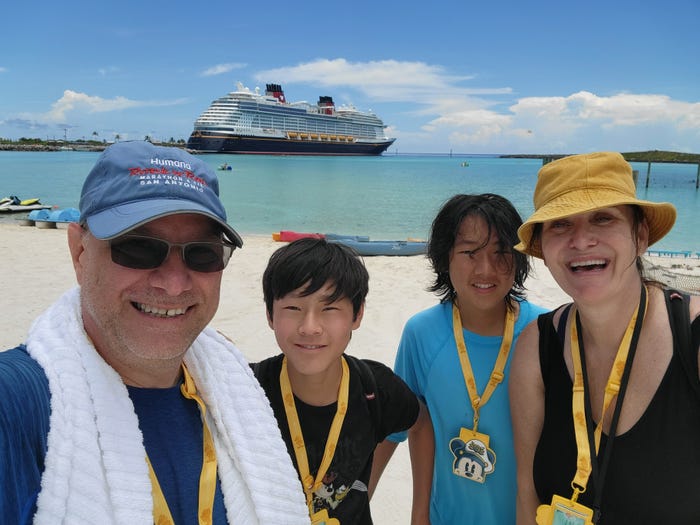 jill and her family posing for a picture on the beach with a cruise ship in the background