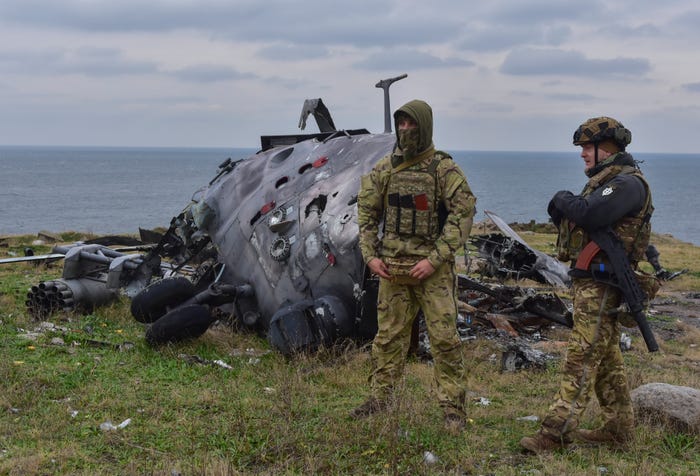 Ukrainian soldiers stand against the background of a damaged Russian military helicopter on Snake Island, in the Black Sea, Ukraine, Sunday, Dec. 18, 2022. 