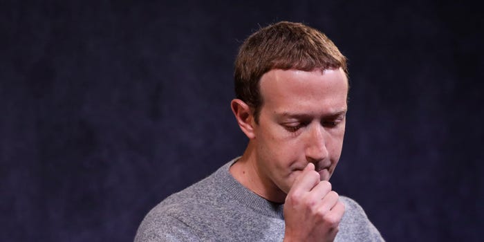Mark Zuckerberg stands with his hand clenched in front of his mouth.