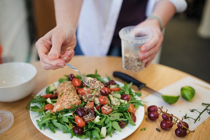 A person sprinkles seeds over a salad.