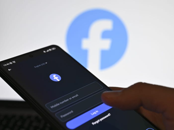 Facebook logo behind a smartphone with the Facebook login screen displayed