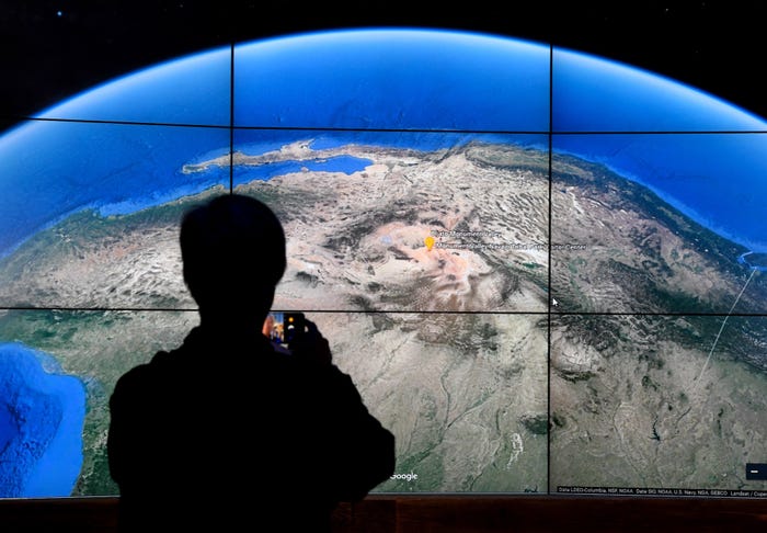 A man's silhouette stands in front of a large screen showing a satellite image from Google Earth.