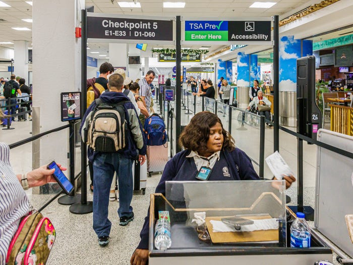 An agent sits scanning passengers in front of a TSA PreCheck sign