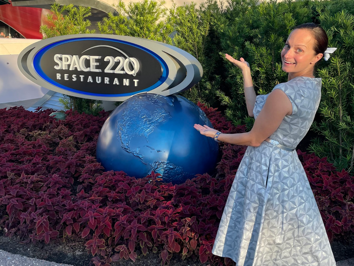 trisha posing with the space 220 sign outside the restaurant in epcot at disney world