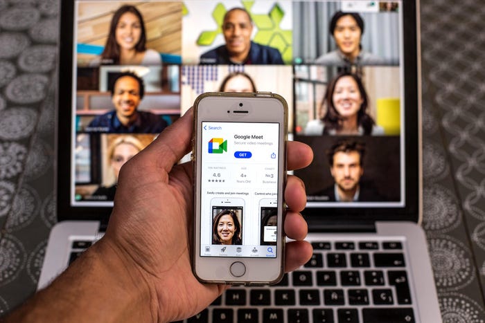 An iPhone displays the Google Meet app on the App Store, while a laptop in the background displays a video conference  call with nine attendees.