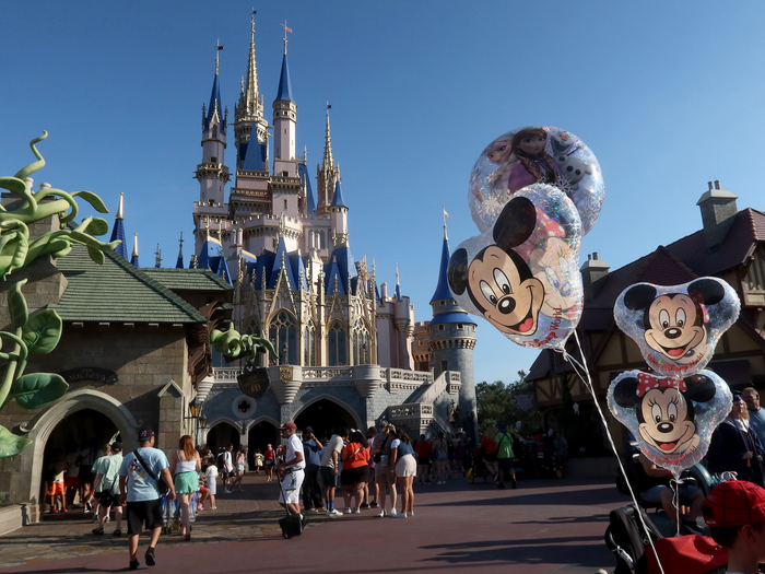 shot of mickey and minnie balloons floating on strollers passing behind cinderella castle at magic kingdom