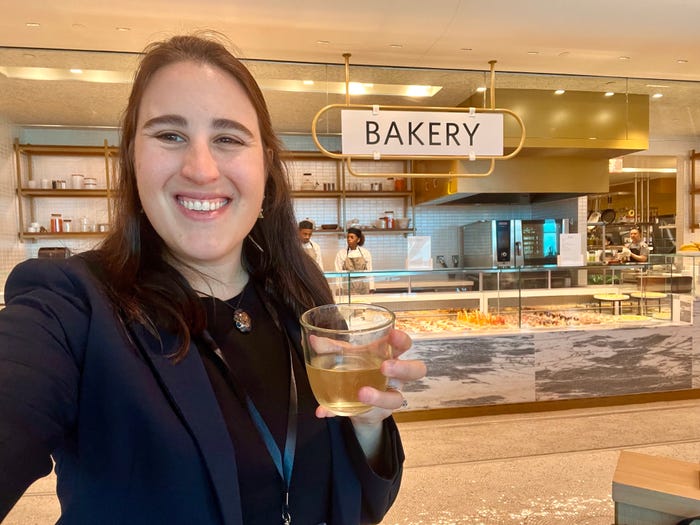 The author standing in front of the bakery at the Delta One Lounge in a blue blazer and holding a glass.