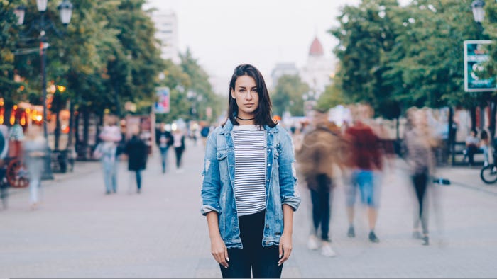 A woman standing in a busy street as people rush by in a blur