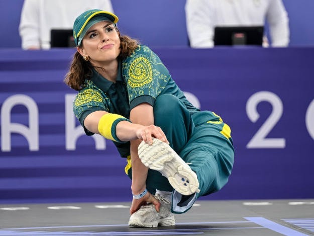 Rachel "Raygun" Gunn competing at the 2024 Paris Olympics, crouching in one leg while she stretches the other leg out and touches her foot with her hand.