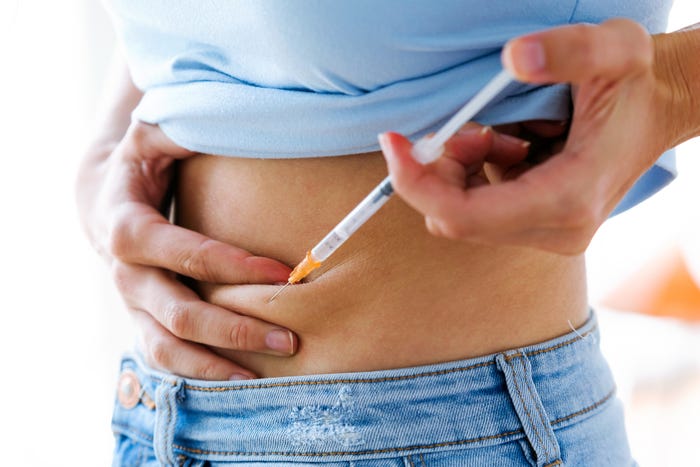 A close up of a woman injecting medication into the skin of her stomach.