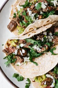 These delicious carne asada tacos are made with grilled skirt steak, avocado, cotija cheese, chopped onion and fresh cilantro. They're super flavorful steak street tacos.