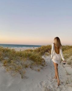 a woman walking down a sandy beach next to the ocean