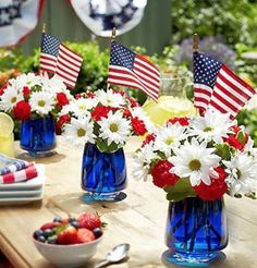 red, white and blue flowers are in vases on a table with american flags