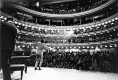 a man standing on top of a stage in front of a large auditorium filled with people