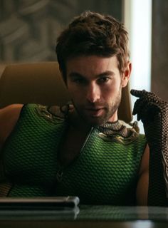a man sitting at a table with a snake on his arm and wearing a green shirt