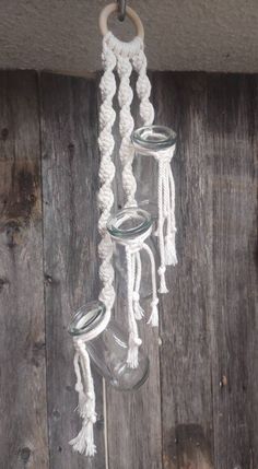 three glass jars hanging from a rope on a wooden wall with wood planks in the background