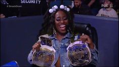 a woman sitting in a chair holding up two wrestling belts and smiling at the camera
