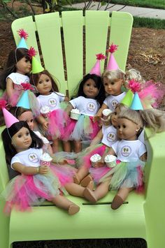 a group of dolls sitting on top of a green chair with birthday hats and cupcakes