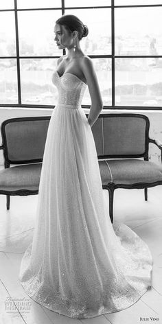 a woman in a wedding dress is standing near a bench and looking out the window