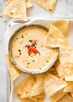 tortilla chips and dip in a bowl on a white plate with some garnish