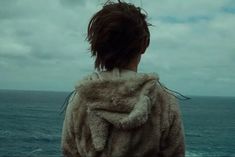 a woman standing in front of the ocean with her back to the camera, looking out at the water