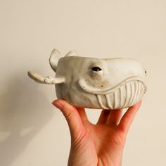 a hand holding a white ceramic whale figurine with its mouth open and it's teeth out