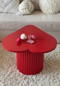 a red table sitting on top of a white rug next to a couch and pillows