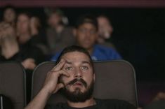 a man with a beard is sitting in a theater and holding his hand up to his face