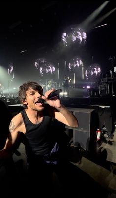 a man singing into a microphone in front of a stage with lots of lights on it