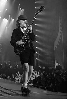 a man in a suit and tie playing an electric guitar on stage with people watching