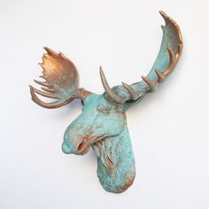 a metal moose head mounted to the side of a wall with copper colored antlers on it