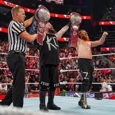 two men standing next to each other holding up their wrestling belts in front of an audience