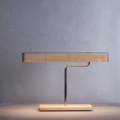 a wooden table with a metal base and a light on it's side, in front of a gray wall