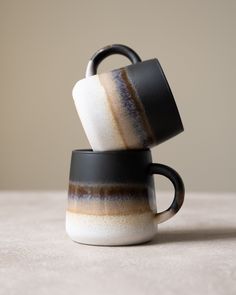 two black and white coffee mugs stacked on top of each other, one with a brown stripe